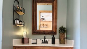 A wooden vanity with a mirror, a sink, and a shelf with toiletries. - Adorable, cozy, waterfront cabin on the River, fish, kayak, tube from property. (Mineral Bluff)