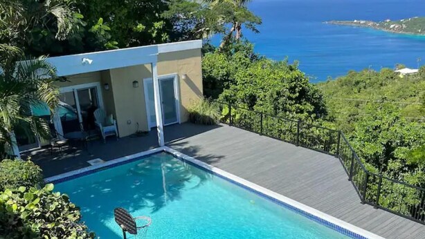 Una piscina con cubierta de madera, rodeada de abundante vegetación y vistas a la costa.