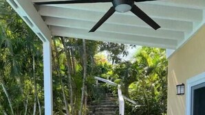 Un espacio al aire libre cubierto con piscina, mesa y sillas, rodeado de abundante vegetación y una escalera que lleva a un nivel superior.