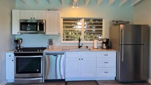 Una cocina moderna con armarios blancos, electrodomésticos de acero inoxidable y un ventanal con vistas al verdor.