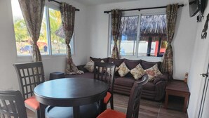 A room with a round table and chairs, a sofa with floral cushions, and a window with curtains. - VILLA CLAUDIAS (Taxisco)