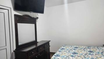A bedroom with a bed, a dresser, a TV mounted on the wall, and a door.