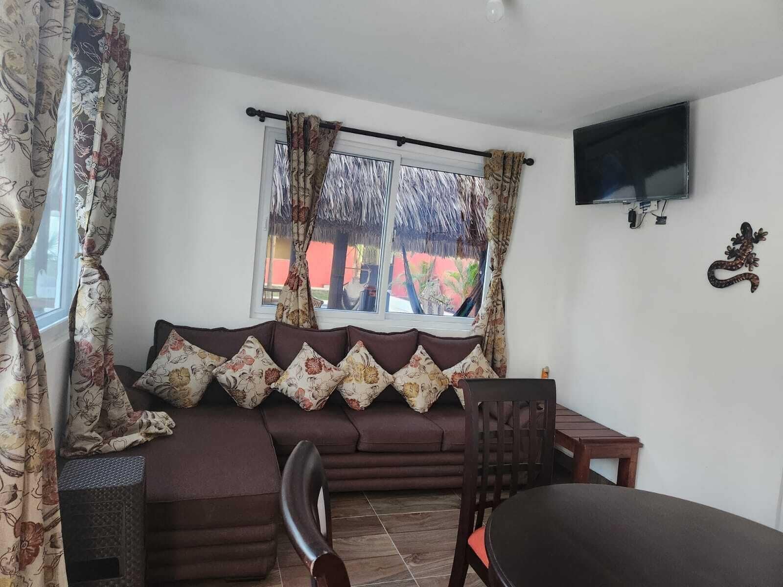 Una sala de estar con un sofá, un televisor montado en la pared y un ventanal con cortinas.