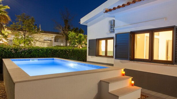 A modern pool area with a rectangular pool, a small set of steps leading to a door, and a well-lit exterior at night. - Portimão: villa with heatable pool & BBQ (Portimão)