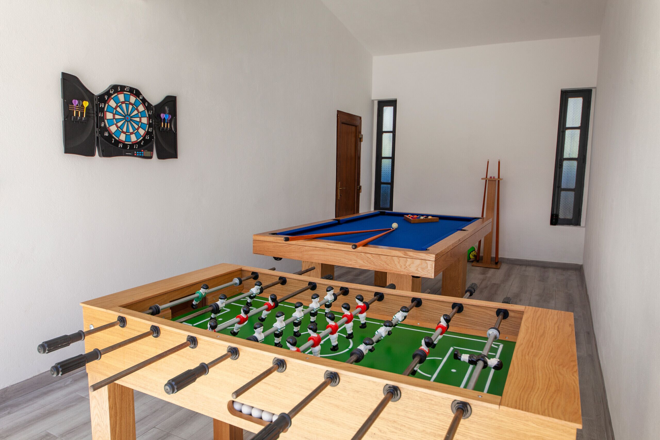 A room with a foosball table, a pool table, and a dartboard.