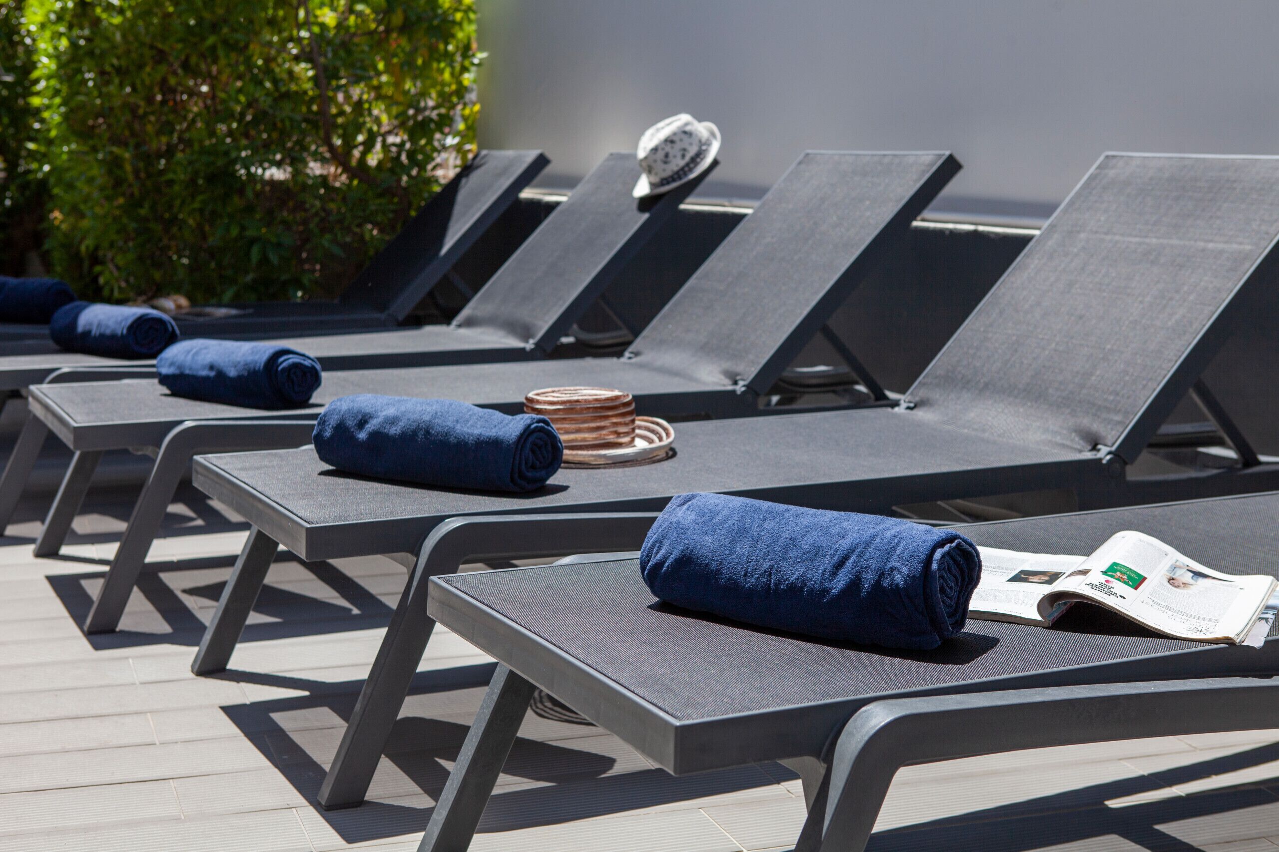 A row of sun loungers with towels and a magazine on them, set on a tiled deck.