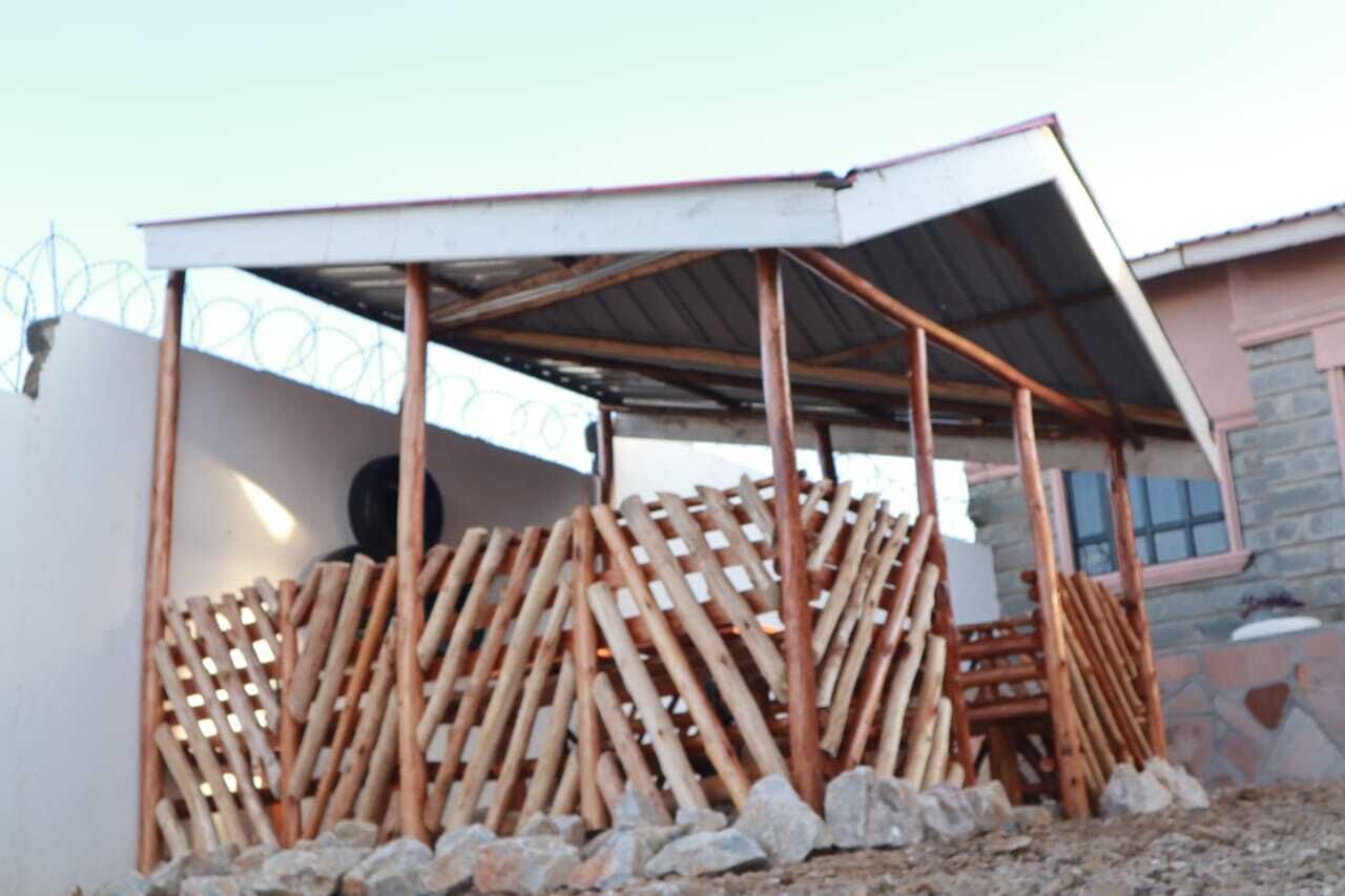 Een constructie met een metalen dak en houten balken, omringd door rotsen en een stenen muur.