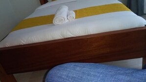 Un lit bien fait, avec une tête de lit en bois, une literie blanche et jaune, et des serviettes enroulées posées sur le lit.