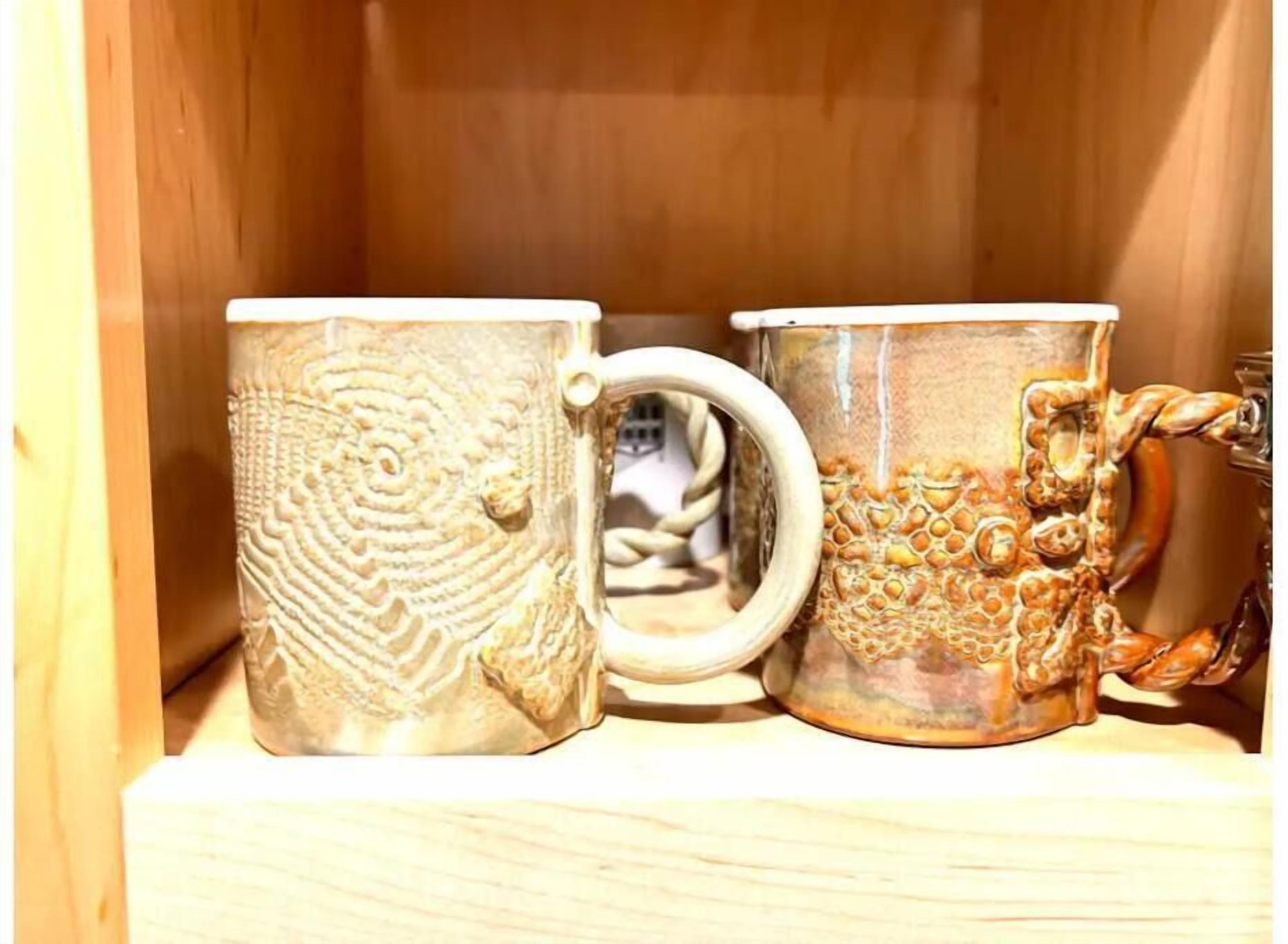 Three ceramic mugs with intricate designs, displayed on a wooden shelf.