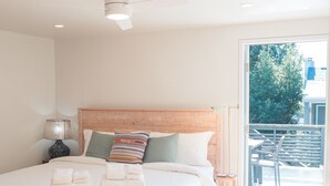 A bedroom with a large bed, a ceiling fan, and a view of the outdoors. - Irie on Erie B (Folly Beach)