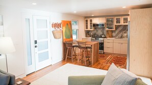 A modern kitchen with wooden cabinets, a microwave, and a stove. There is a dining area with a table and chairs. - Irie on Erie B (Folly Beach)