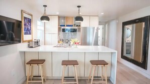 Een moderne keuken met een centraal eiland, drie barkrukken, hanglampen en een grote spiegel aan de muur.