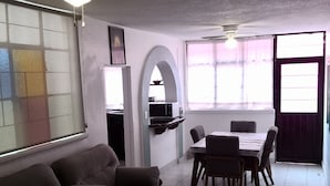 Un salon avec un canapé, une table à manger avec des chaises, un coin cuisine et une grande fenêtre avec des rideaux.