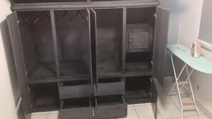 Une pièce avec une armoire noire, une petite table avec un fer à repasser et un sol carrelé.