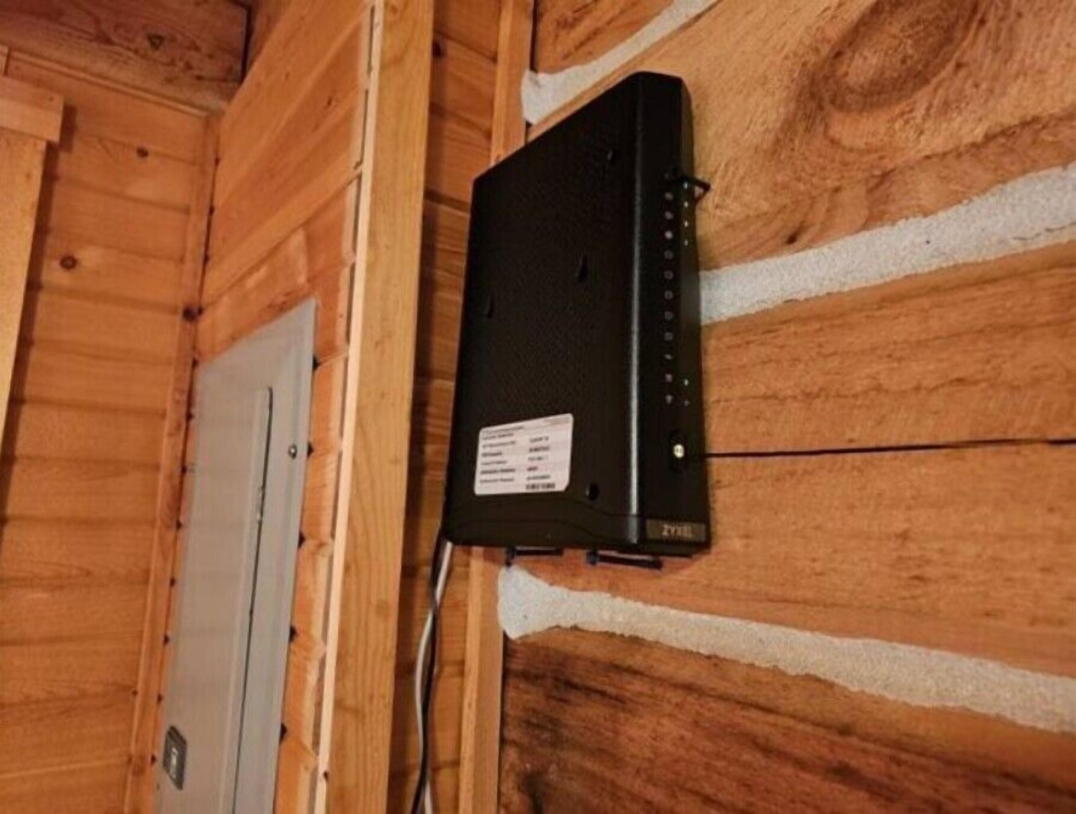 Een zwart elektronisch apparaat bevestigd aan een houten wand, met een label en een kabel.