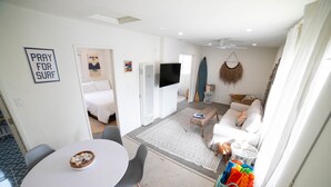 En moderne stue med en hvid sofa, et spisebord med stole, et fjernsyn og en surfbræt på væggen.