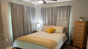Een slaapkamer met een bed, nachtkastje, kapstok en plafondventilator.