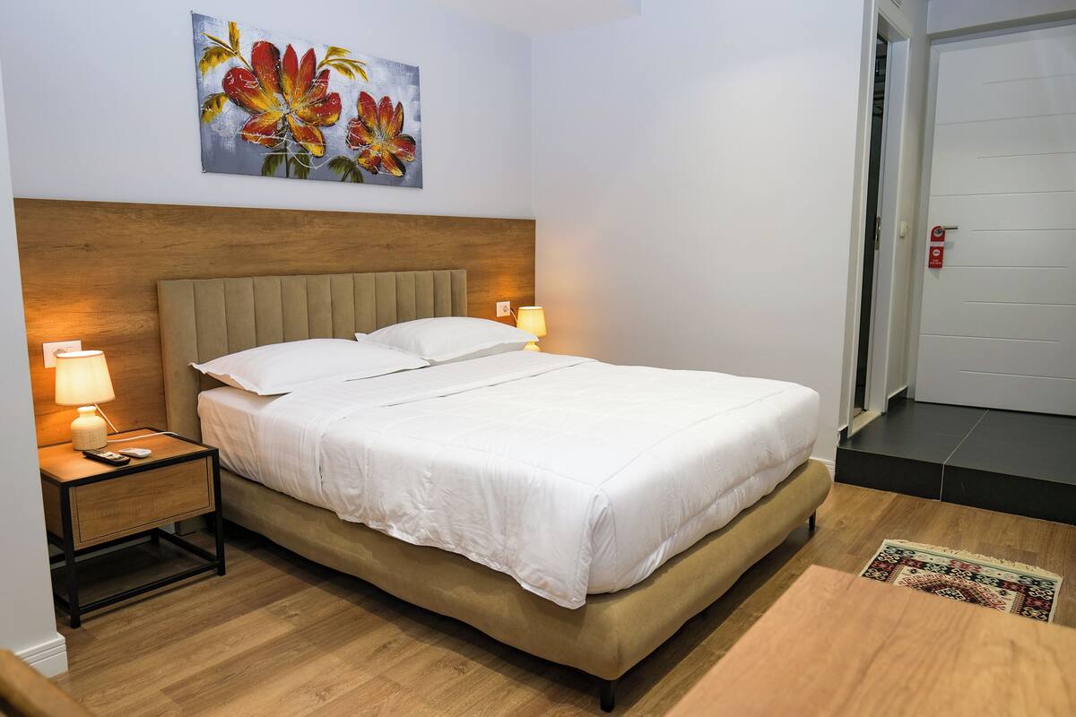 A neatly made bed with white linens, a wooden headboard, and two bedside lamps.