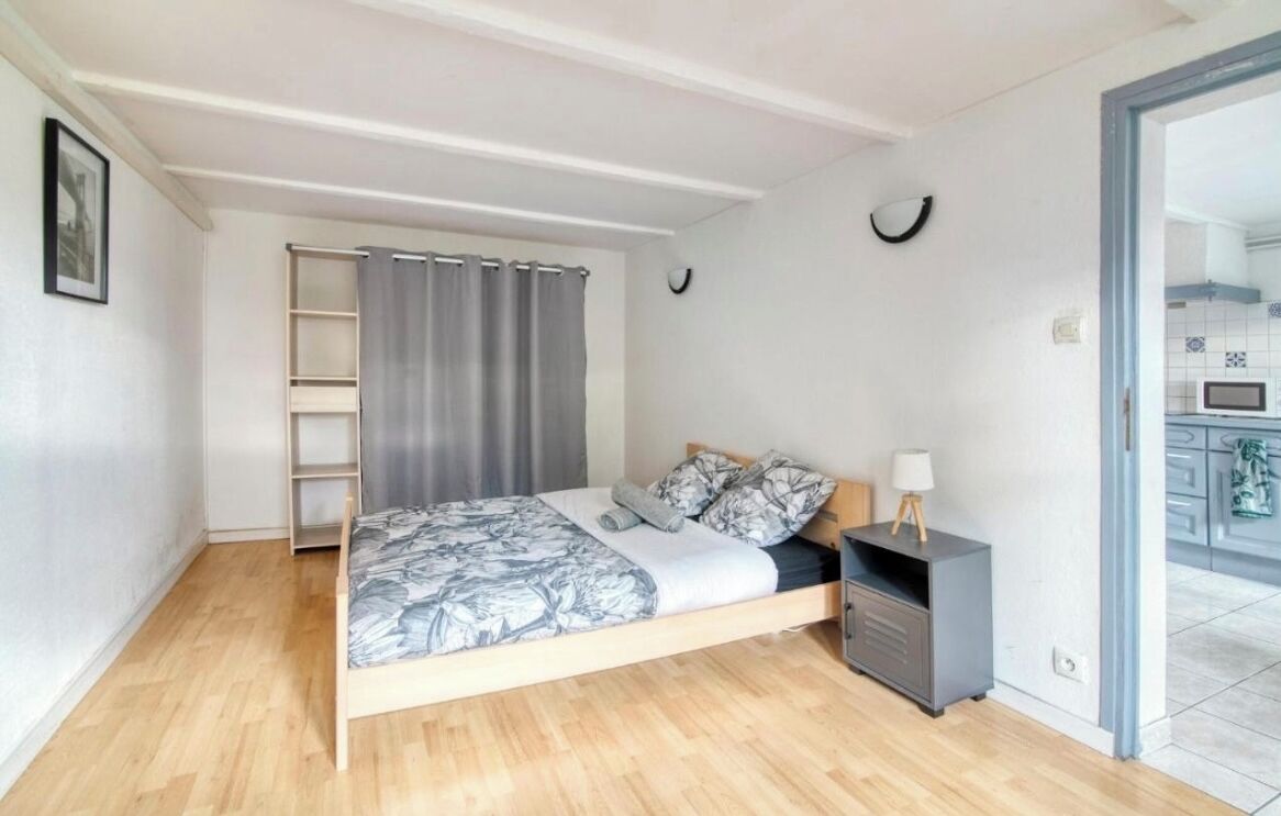 A bedroom with a bed, a bedside table, a wardrobe, and a view of a kitchen.