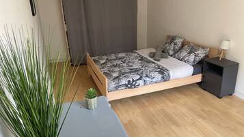 Un dormitorio con cama, mesita de noche, planta en maceta y cortina.