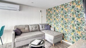 A modern living room with a grey sectional sofa, a small round coffee table, and a tropical leaf-patterned wall. - Apparemment à Côté du Meet (Cornebarrieu)