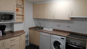 A compact kitchen with a microwave, washing machine, and stove. - Funcional Apartamento en Iturrama (Pamplona)