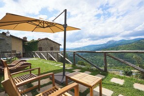 A terrace with wooden furniture, a table, and an umbrella, overlooking a mountainous landscape. - "Historic Sillico Relais - Hot Tub, Sauna&Charme" (Sillico)