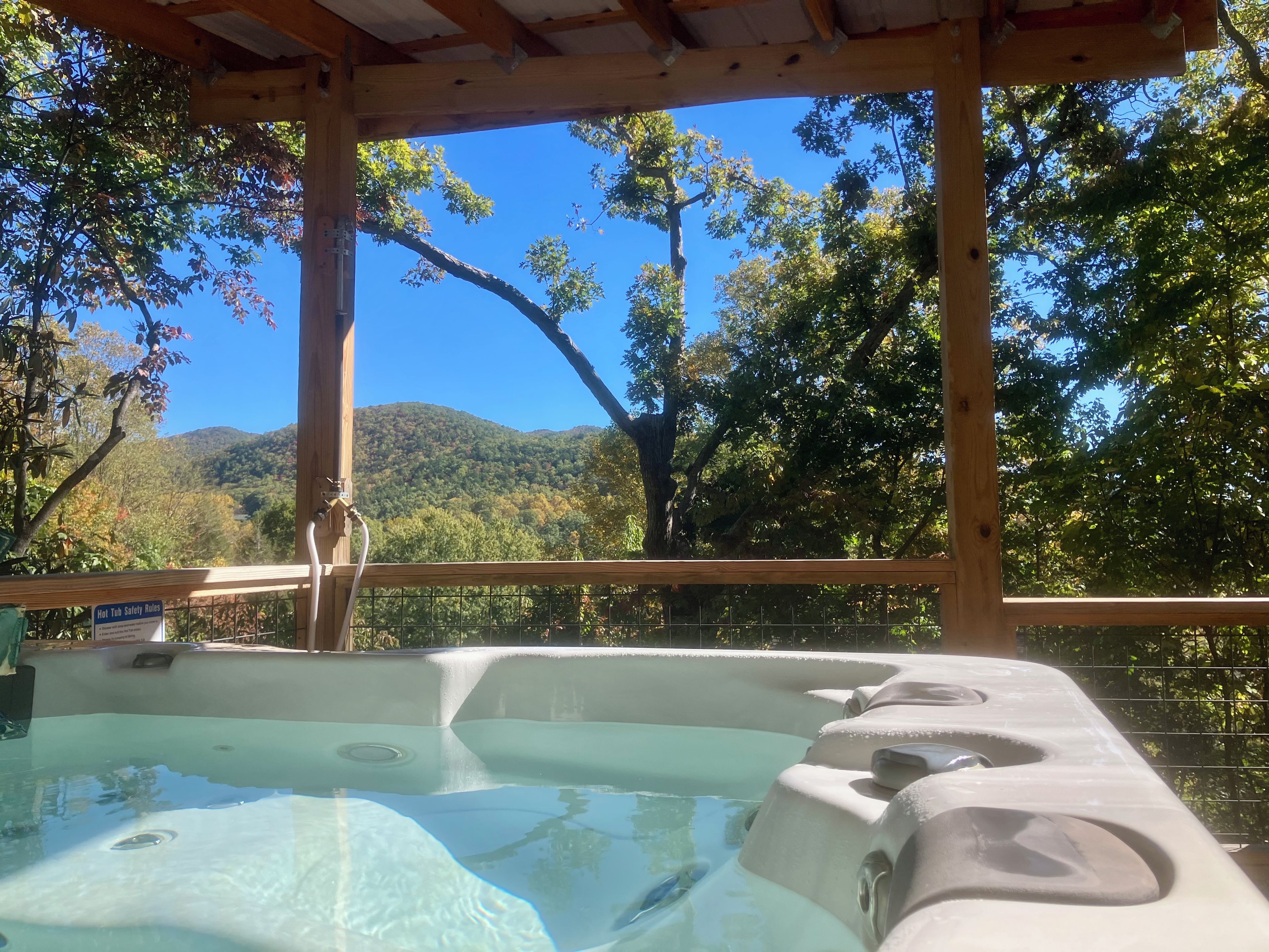 Un bain à remous avec une terrasse en bois et une vue sur une colline boisée.