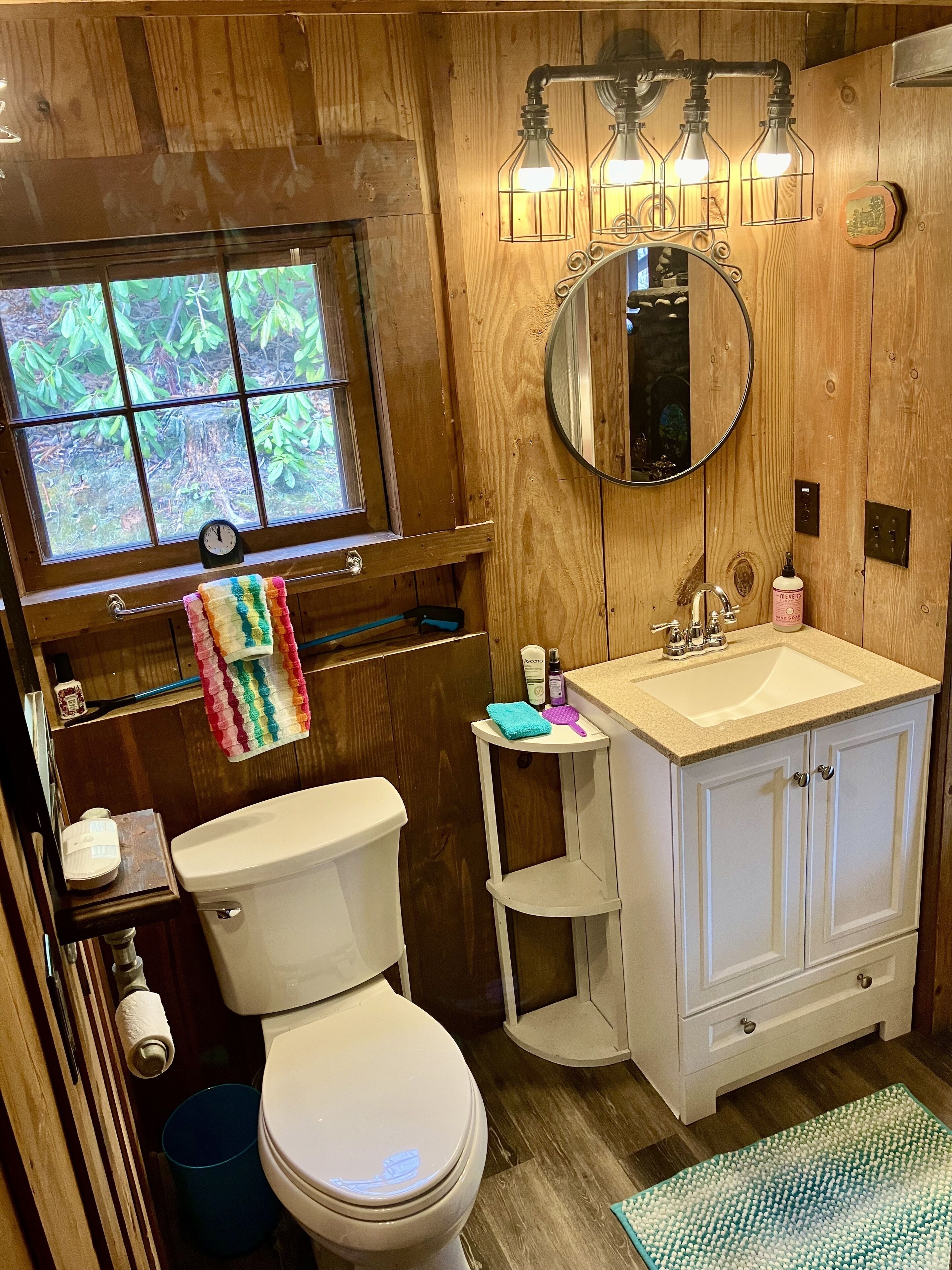 Ein kleines Badezimmer mit Toilette, Waschbecken mit Spiegel und einem Fenster mit Blick auf Grünflächen.