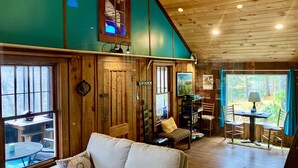 Un accogliente interno di una baita con soffitto in legno, un divano, un tavolo da pranzo e vista sulla foresta dalle finestre.