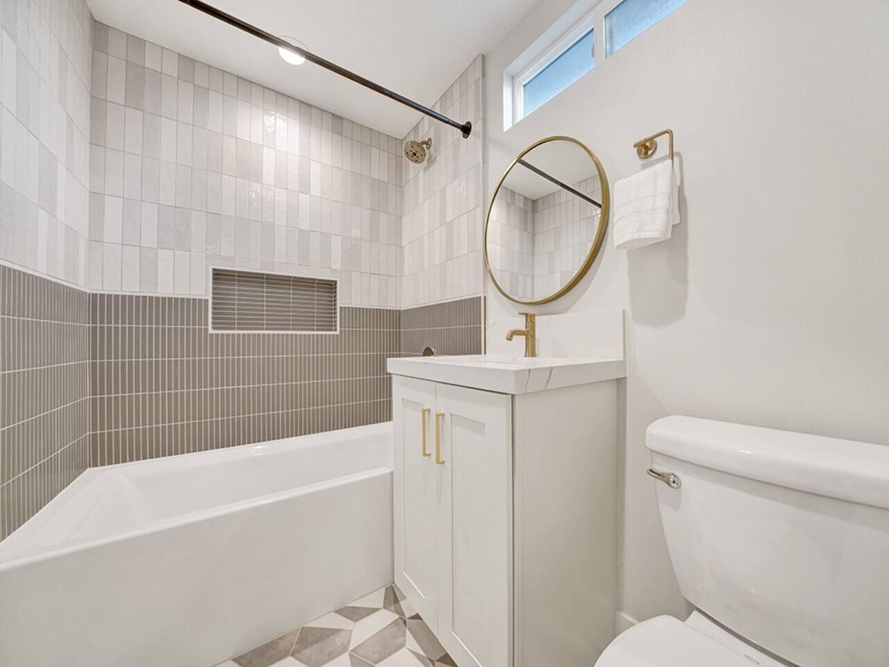 A bathroom with a bathtub, toilet, vanity with a mirror, and a window.
