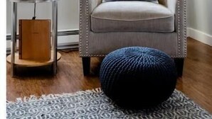 Une pièce d’angle avec un fauteuil gris, une petite table ronde avec une lampe et une fenêtre donnant sur des arbres.