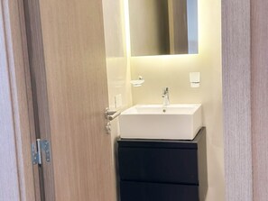 Un baño con lavamanos blanco, espejo y mueble negro.