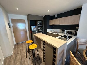 A compact kitchen with a central island, two stools, and a microwave.