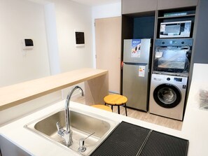 Una kitchenette compacta con un lavamanos de acero inoxidable, un microondas integrado, un refrigerador y una lavadora.