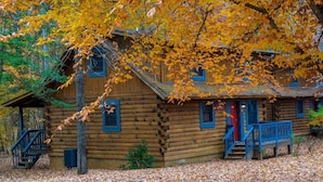 A rustic log cabin with a porch, surrounded by autumn foliage. - Wilderness Presidential Resort Cabins (Spotsylvania)