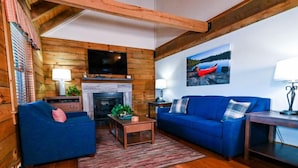 A cozy log cabin interior with a fireplace, blue furniture, and a painting of a boat on the wall. - Wilderness Presidential Resort Cabins (Spotsylvania)