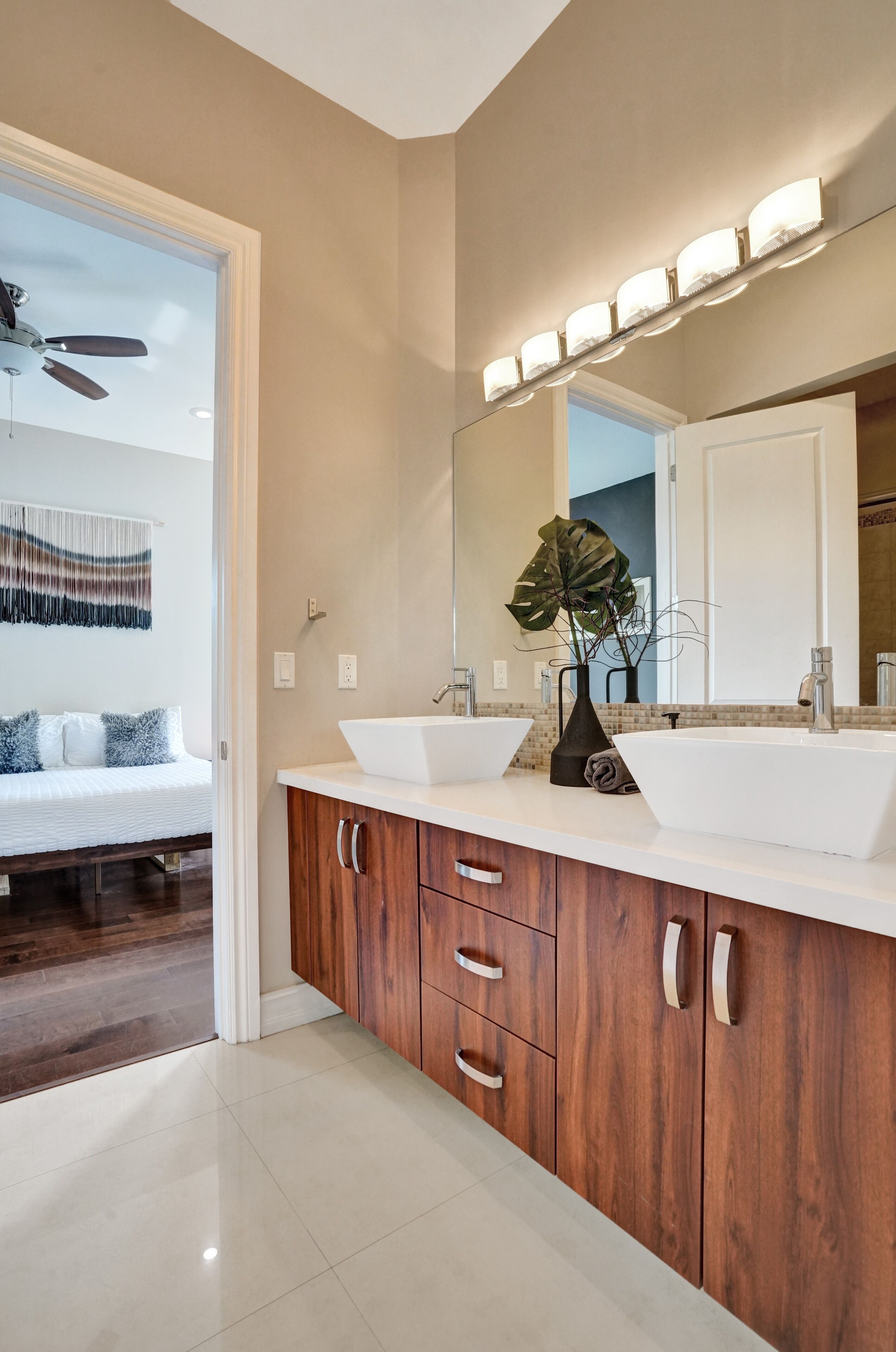 A modern bathroom with a large mirror, two vessel sinks, wooden cabinets, and a ceiling fan.