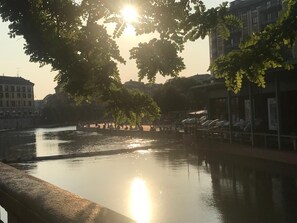 A calm river with a bridge in the foreground, surrounded by trees and buildings. - Dockside Studio (Milano)