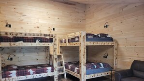 Eine Hütte mit drei Etagenbetten, Holzboden, Schreibtisch mit Stuhl und einem kleinen Tisch mit Korb.