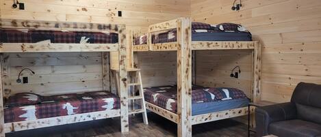 A cabin with three bunk beds, a wooden floor, a desk with a chair, and a small table with a basket.