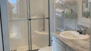 A bathroom with a glass shower enclosure, a toilet, a sink with a marble countertop, and a towel rack with folded towels.