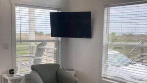 A living room with a grey armchair, a small table with a bowl, and a flat-screen TV mounted on the wall.