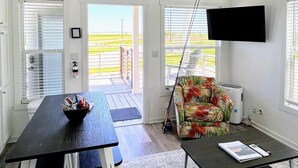 A spacious living room with a ceiling fan, a TV mounted on the wall, a dining table, and a sofa. - The Spoonbill Guest House at Goose Island Flats 1BR 1BA (Rockport)