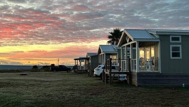 A row of mobile homes with a grassy field and a sunset in the background. - The Spoonbill Guest House at Goose Island Flats 1BR 1BA (Rockport)