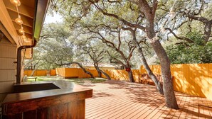 Une terrasse en bois dotée d’un bar intégré, entourée d’arbres et bordée d’un mur jaune.