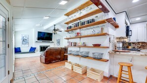 Une cuisine avec des étagères en bois, un téléviseur et un coin salon comprenant un canapé et des coussins.