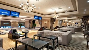 A hotel lobby with a bowling alley, seating areas, and a large screen displaying a car show.
