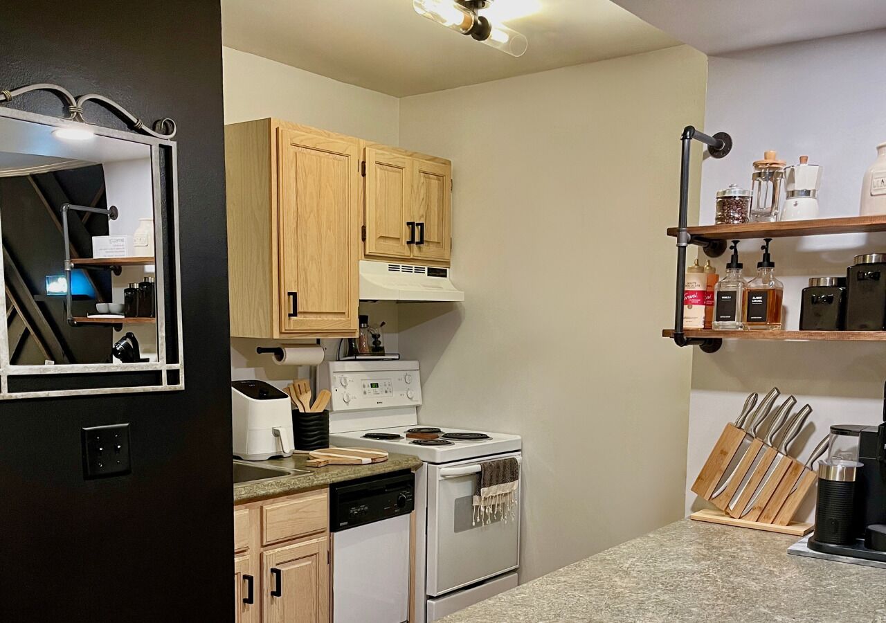 Une cuisine compacte avec des meubles en bois, un four encastré, une plaque de cuisson et une machine à café.