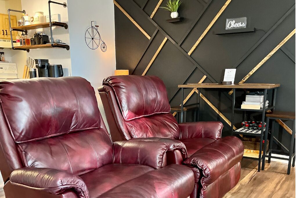 A modern living area with a dark geometric wall design, a red leather sofa, and a small table with a chessboard.